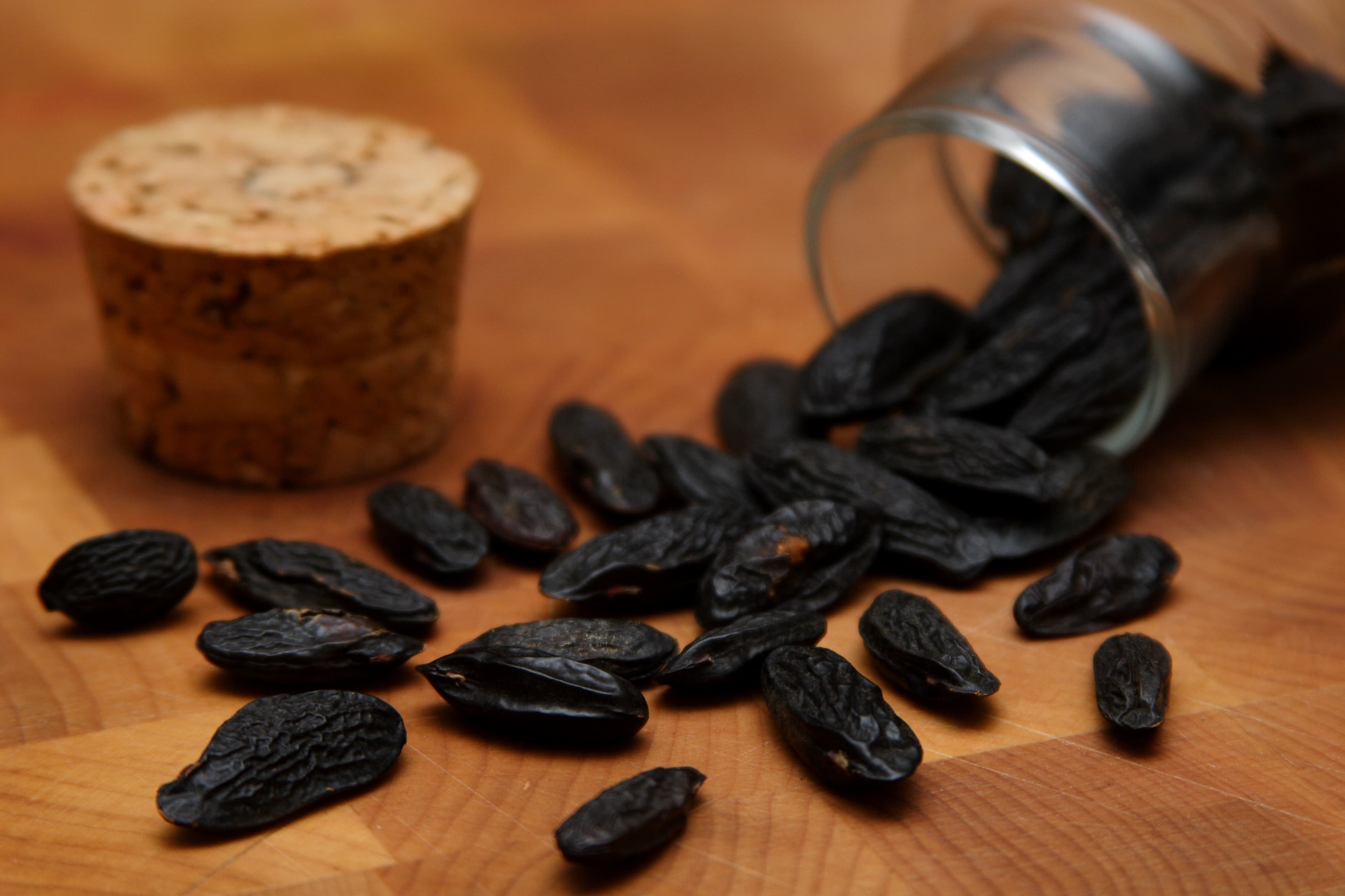 Dried dark tonka beans spilled from a glass jar onto a wooden surface